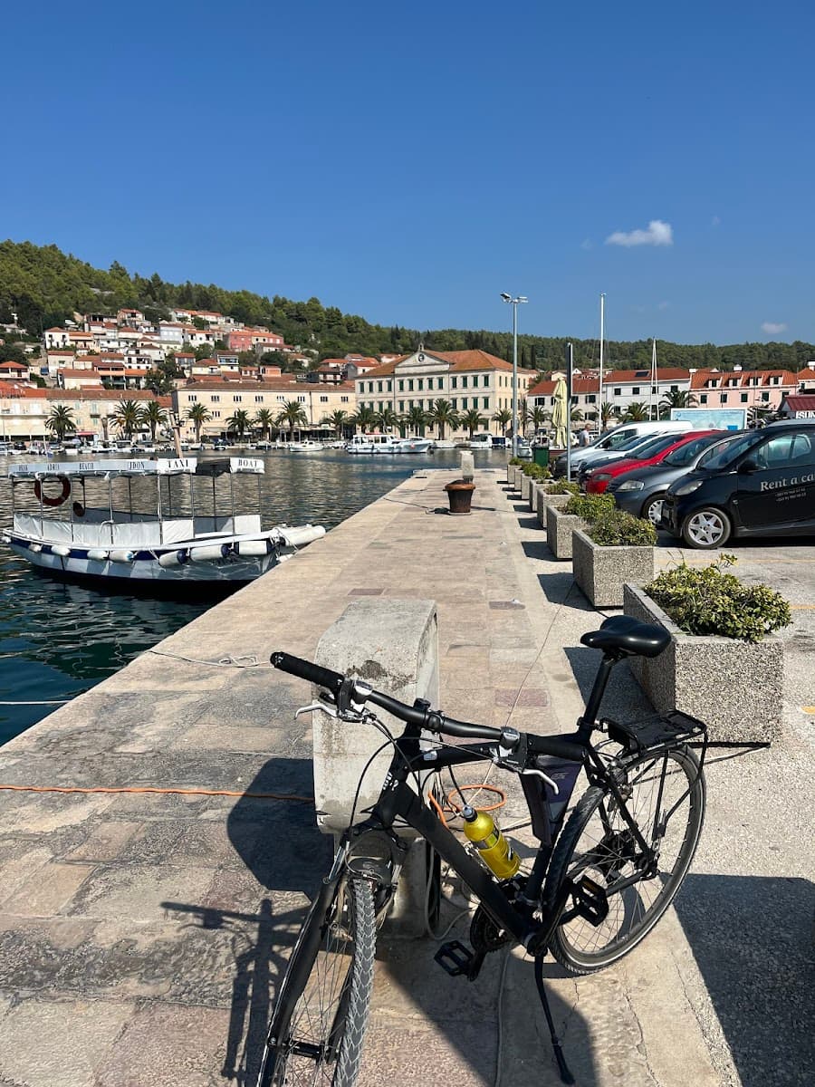 Bicycle parked on stone pier overlooking harbor with town and green hillside in background