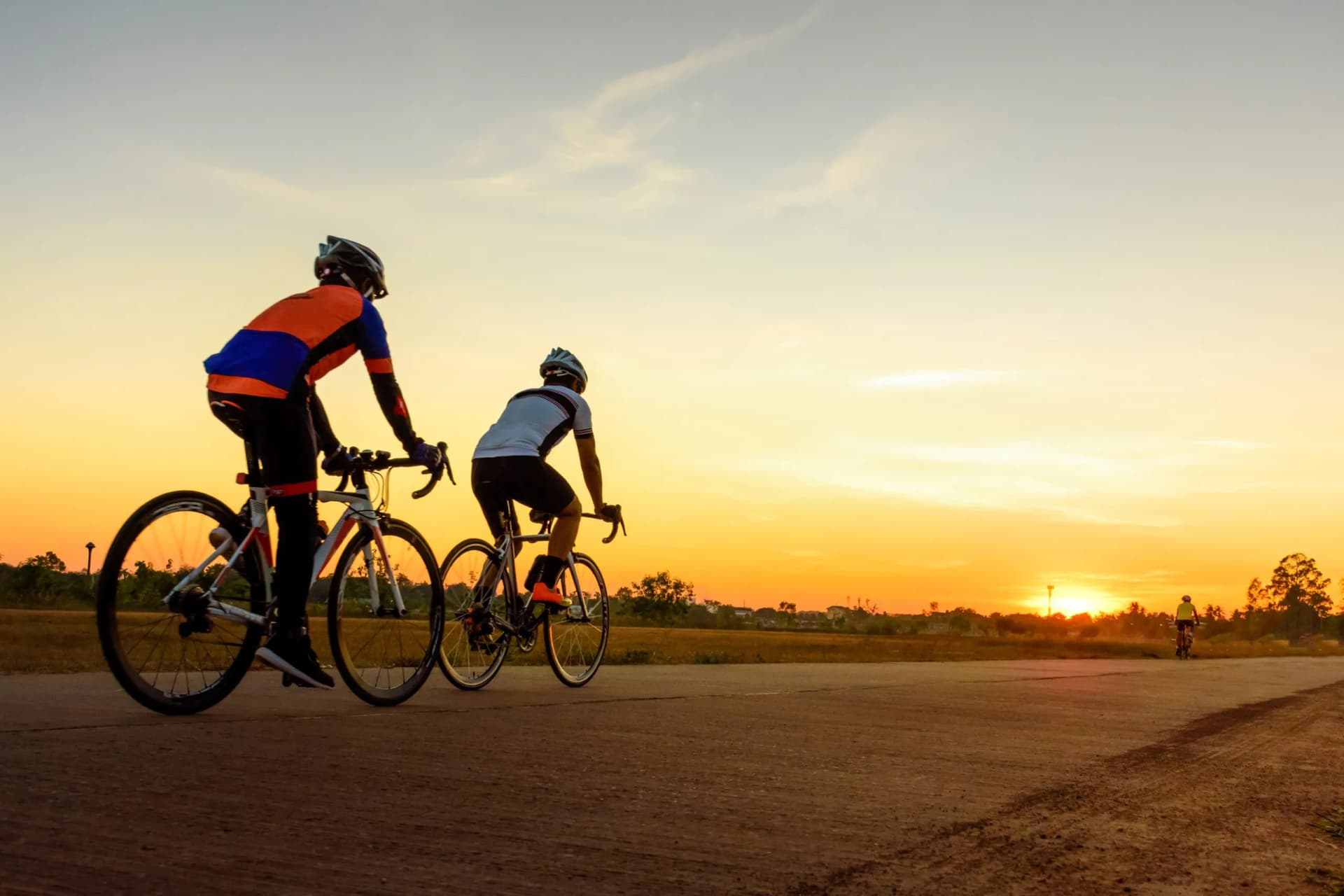 Men ride bicycles on the road with beautiful colorful sunset sky. Sport and active life concept.