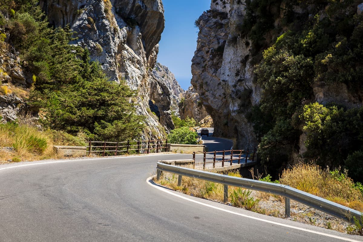 Winding road through Kotsifou Gorge with steep rocky walls and dense green vegetation.