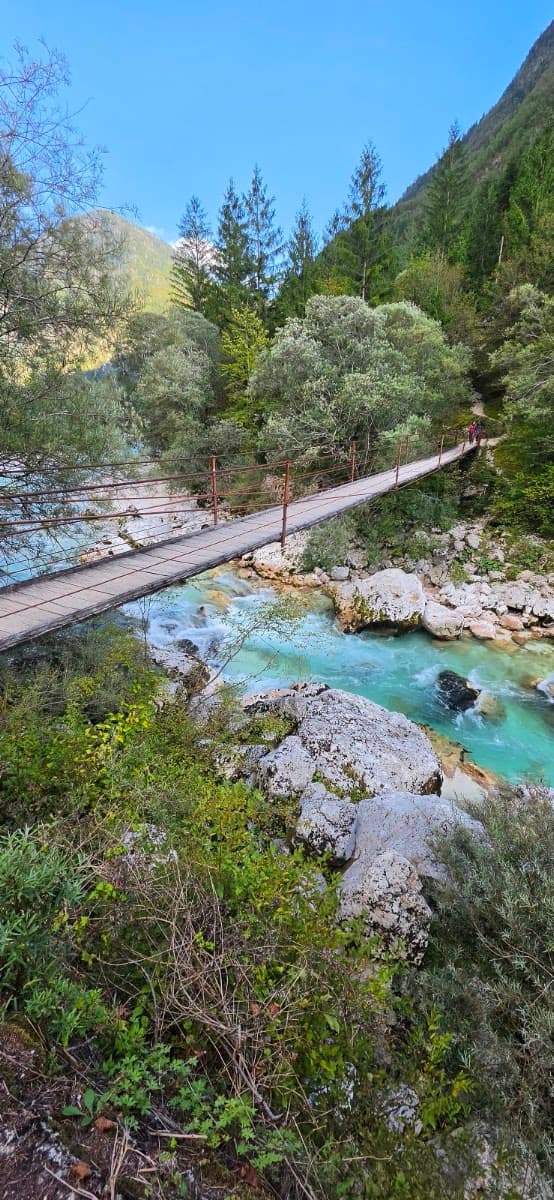 Suspension bridge over turquoise mountain river with forest and rocks