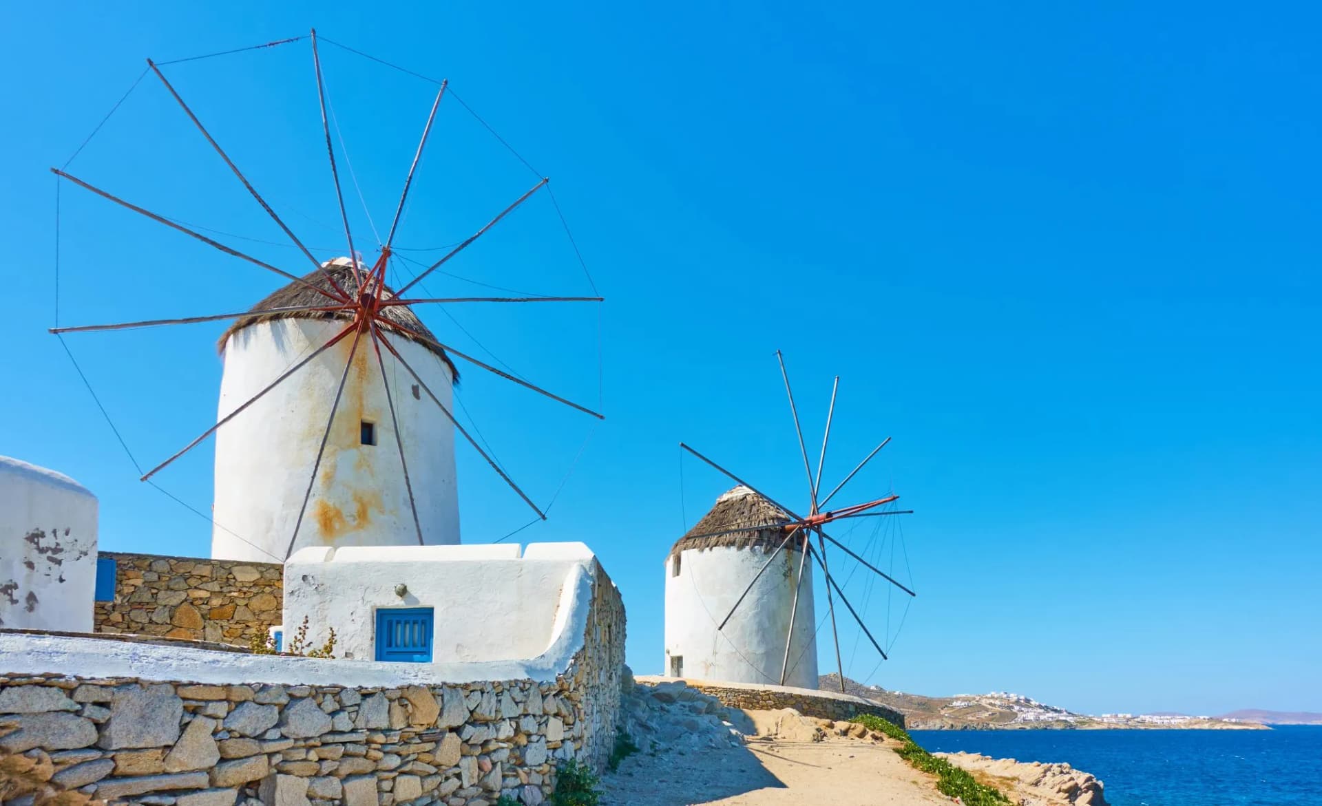 White windmills by the sea in Mykonos under a clear blue sky.