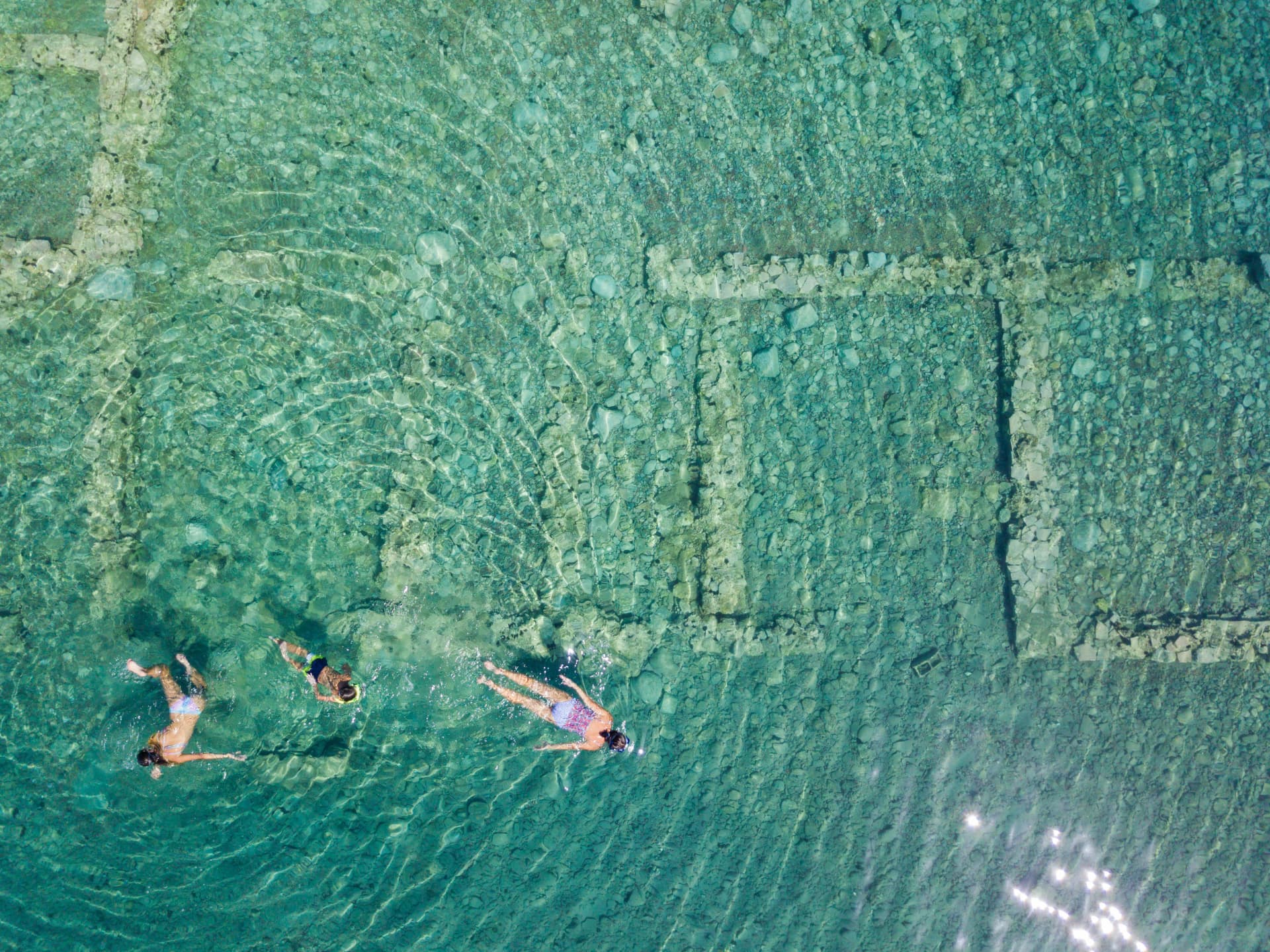 Aerial drone bird's eye view photo of tourists snorkeling above old Sunken City of Epidauros, Greece