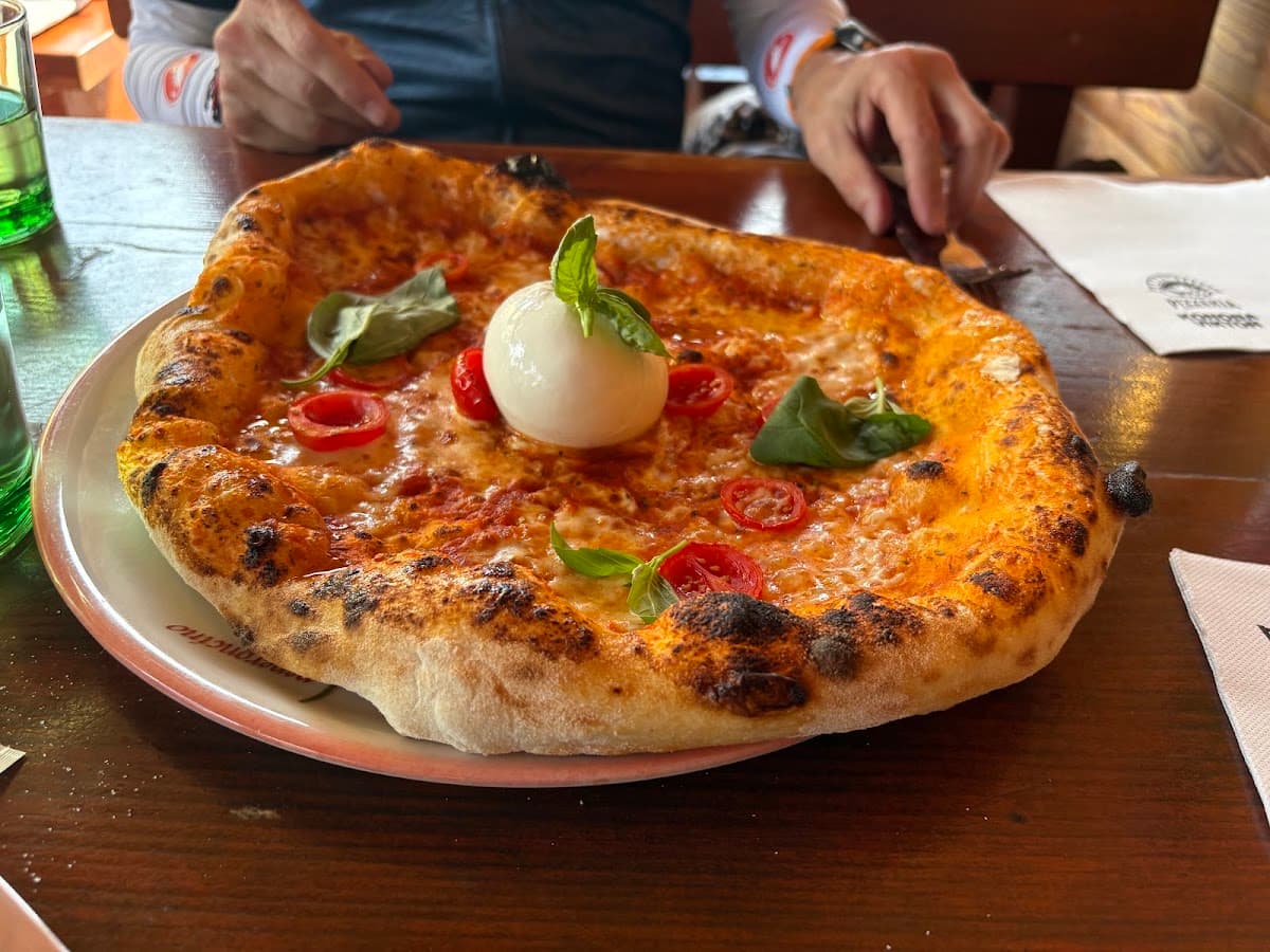 Wood-fired pizza topped with burrata cheese, cherry tomatoes, and fresh basil on wooden table